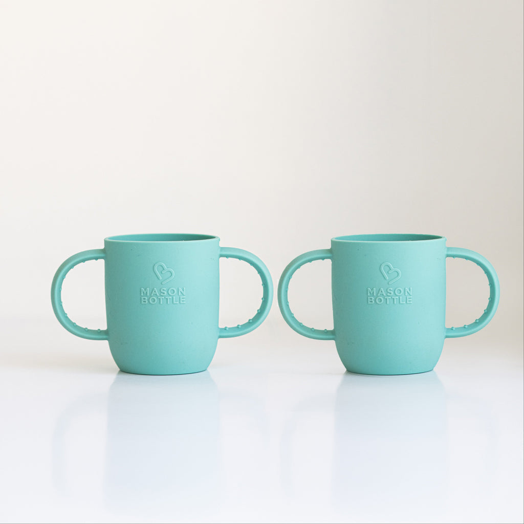 Two turquoise silicone sleeves for baby bottle on a white background