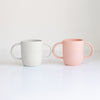 Two baby bottle silicone sleeves, one white and one pink, on a light gray background